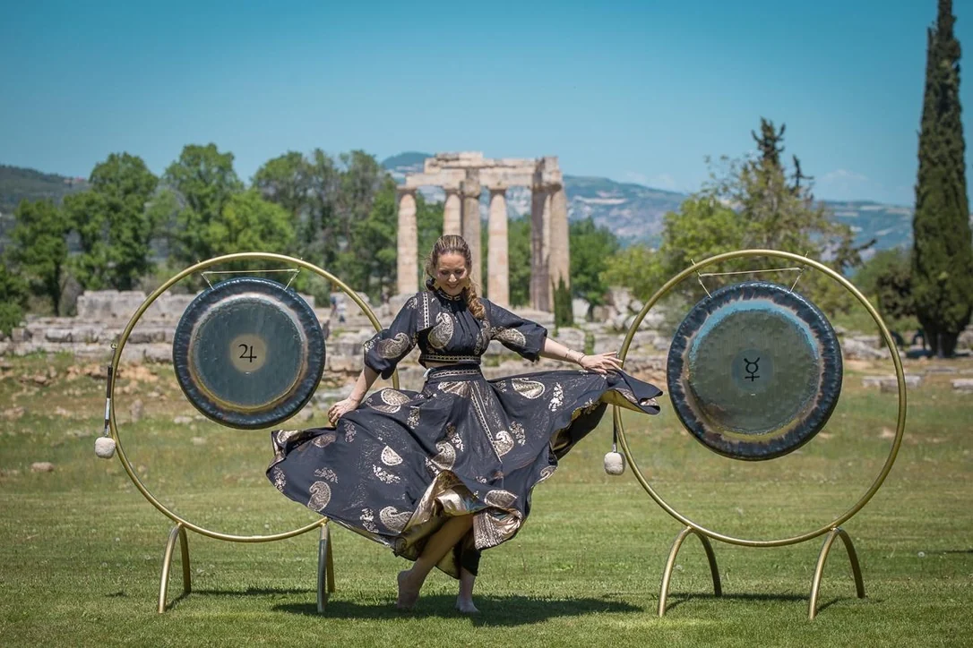 Loukia Papa dancing between planetary gongs before the Temple of Zeus at Ancient Nemea