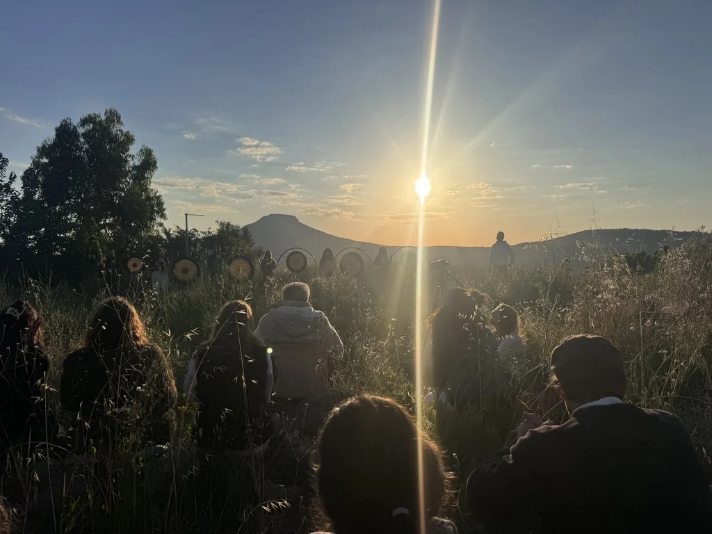 A circle seated in the long grass as the sun rises over the hills, the gongs waiting before them
